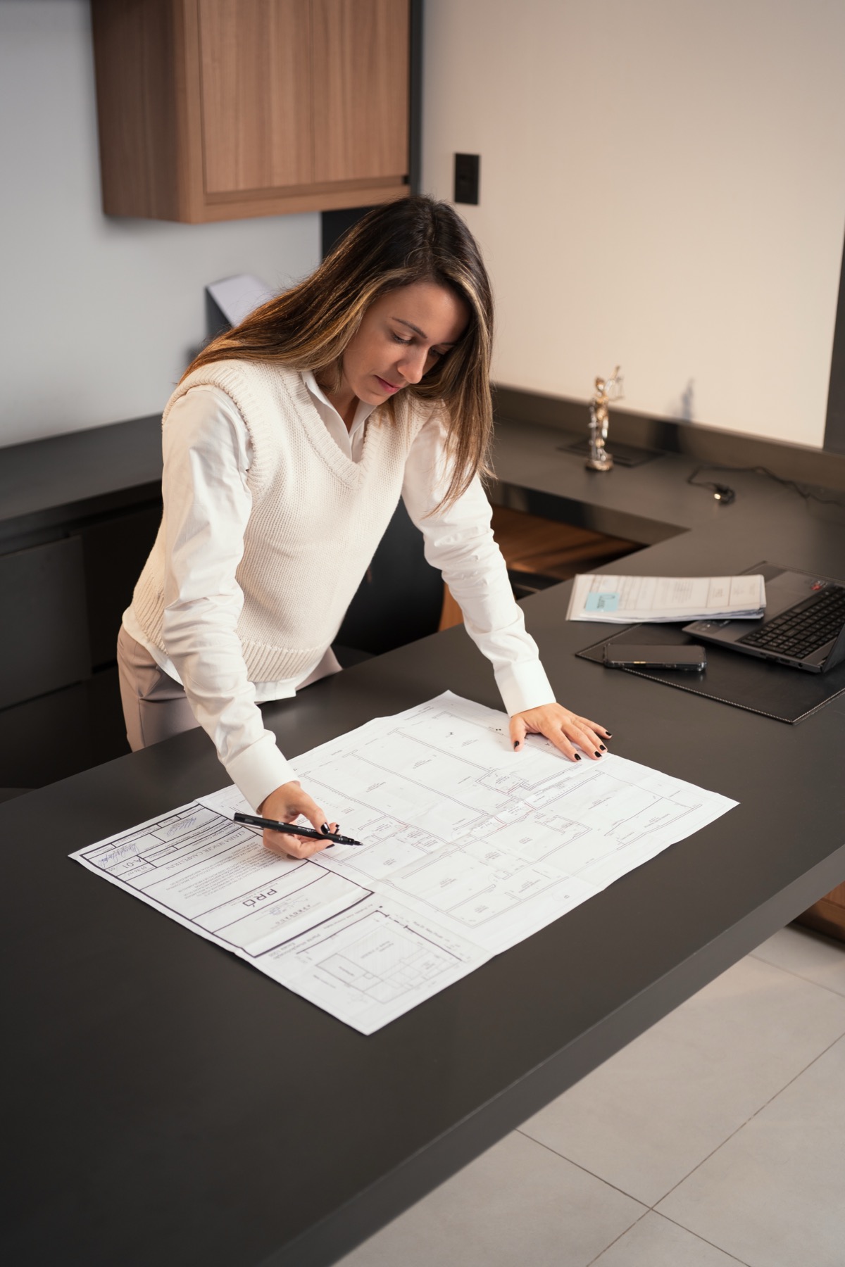 Anny examinando a planta de um imóvel na mesa do escritório