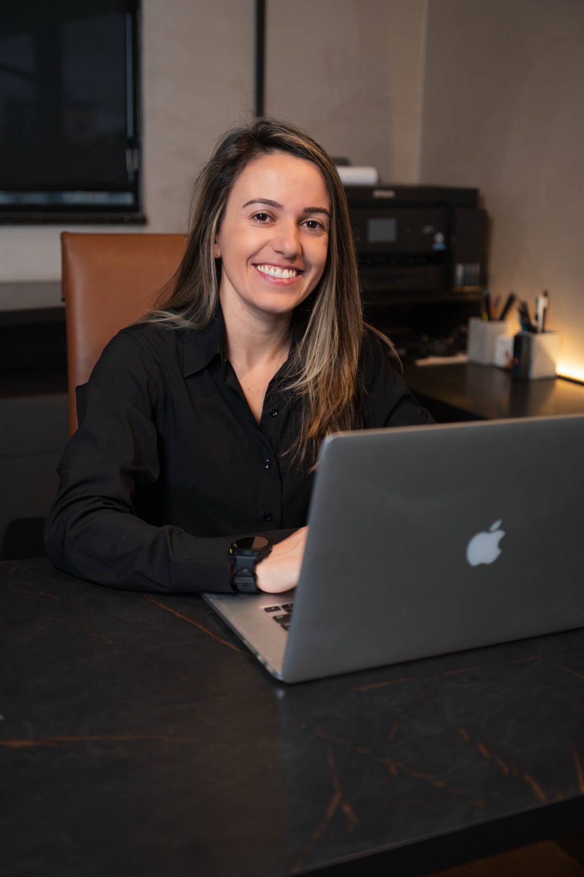 Anny trabalhando à mesa com notebook no escritório em Navegantes